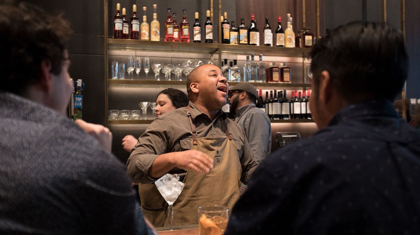 Man in apron laughing among other people in bar setting