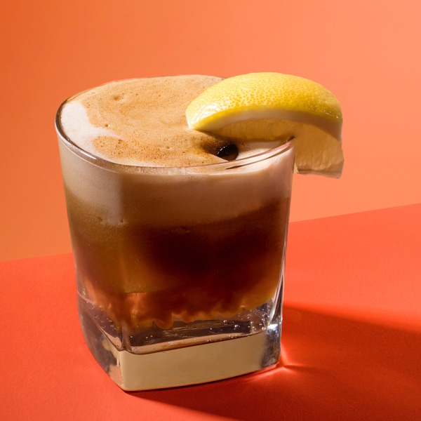 Foamy brown beverage in a tumbler glass in front of an orange background