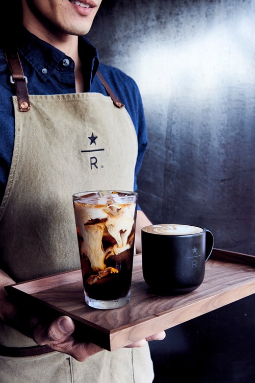 Closeup of person wearing Starbucks Reserve apron, holding a tray of one iced coffee and one hot coffee