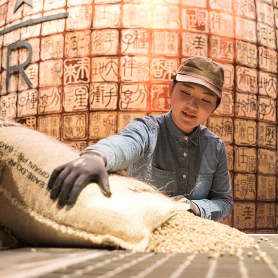 Starbucks Reserve employee handling burlap sack of unroasted coffee beans, in front of a background with Chinese characters