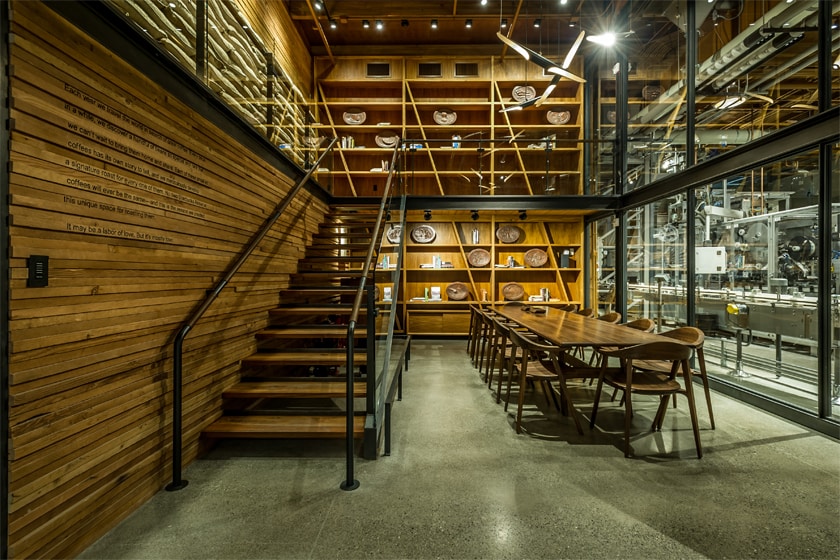 Large wood conference table and chairs, stairs leading to a lofted space, with bookshelves in the background.