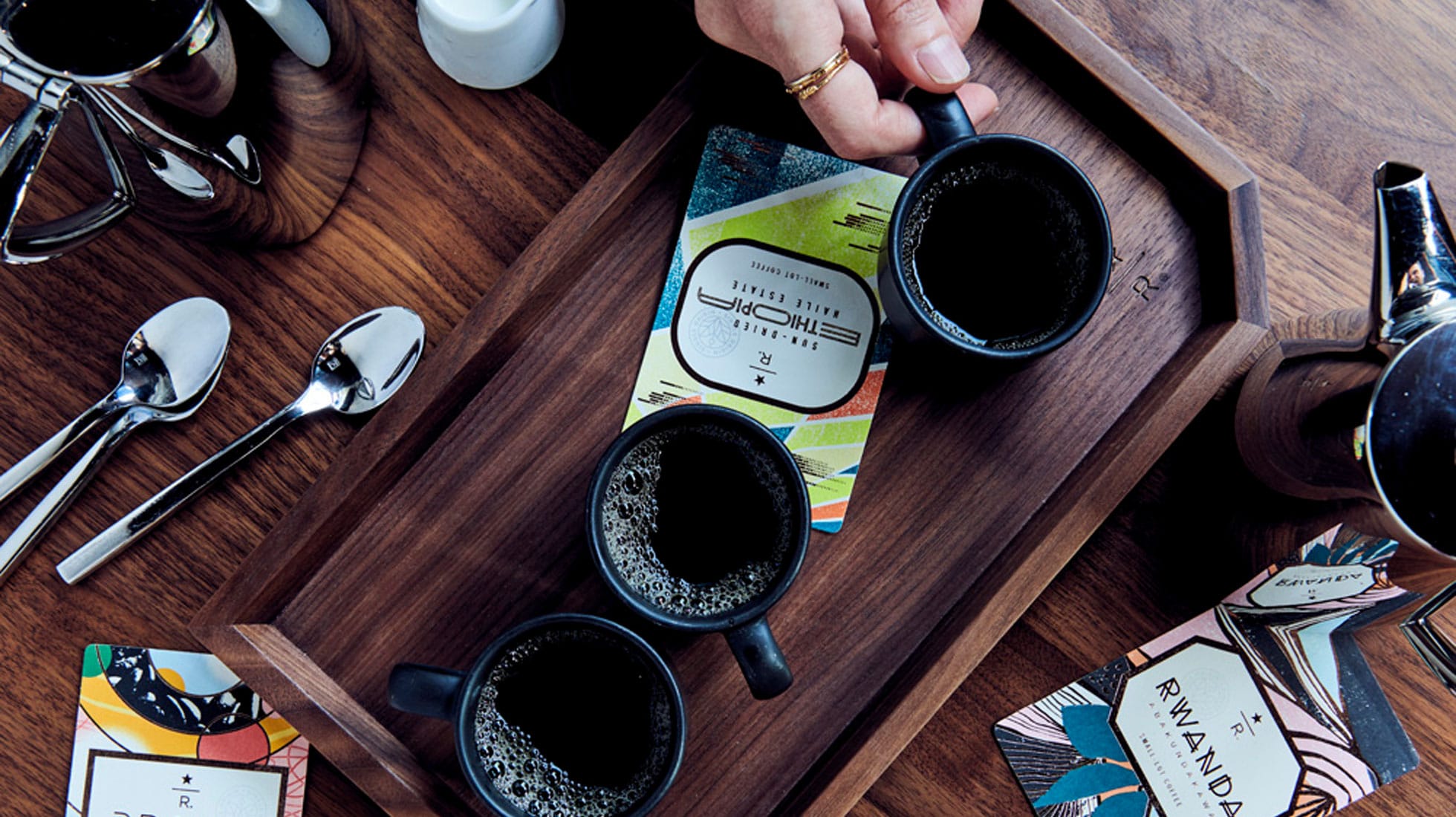 Overhead shot of multiple cups of coffee on a tray with coffee cards, as well as spoons and pots