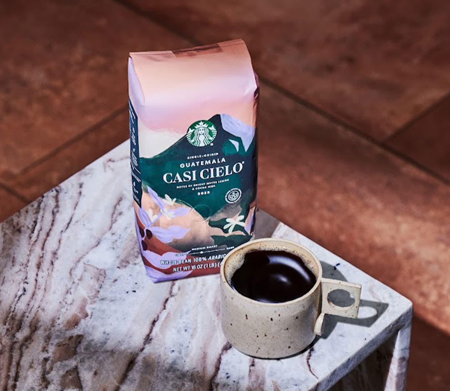 A bag of whole bean coffee with a mountain design next to a mug of hot coffee