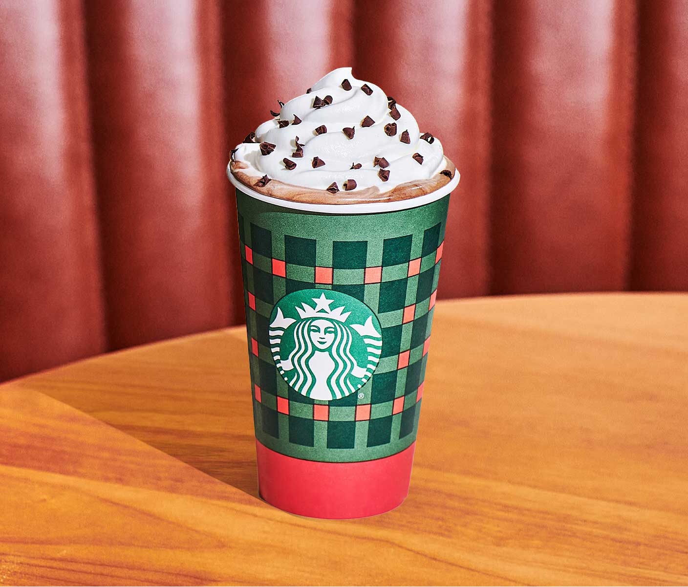 A hot coffee drink in a red and green Starbucks cup topped with whipped cream and brown sprinkles.