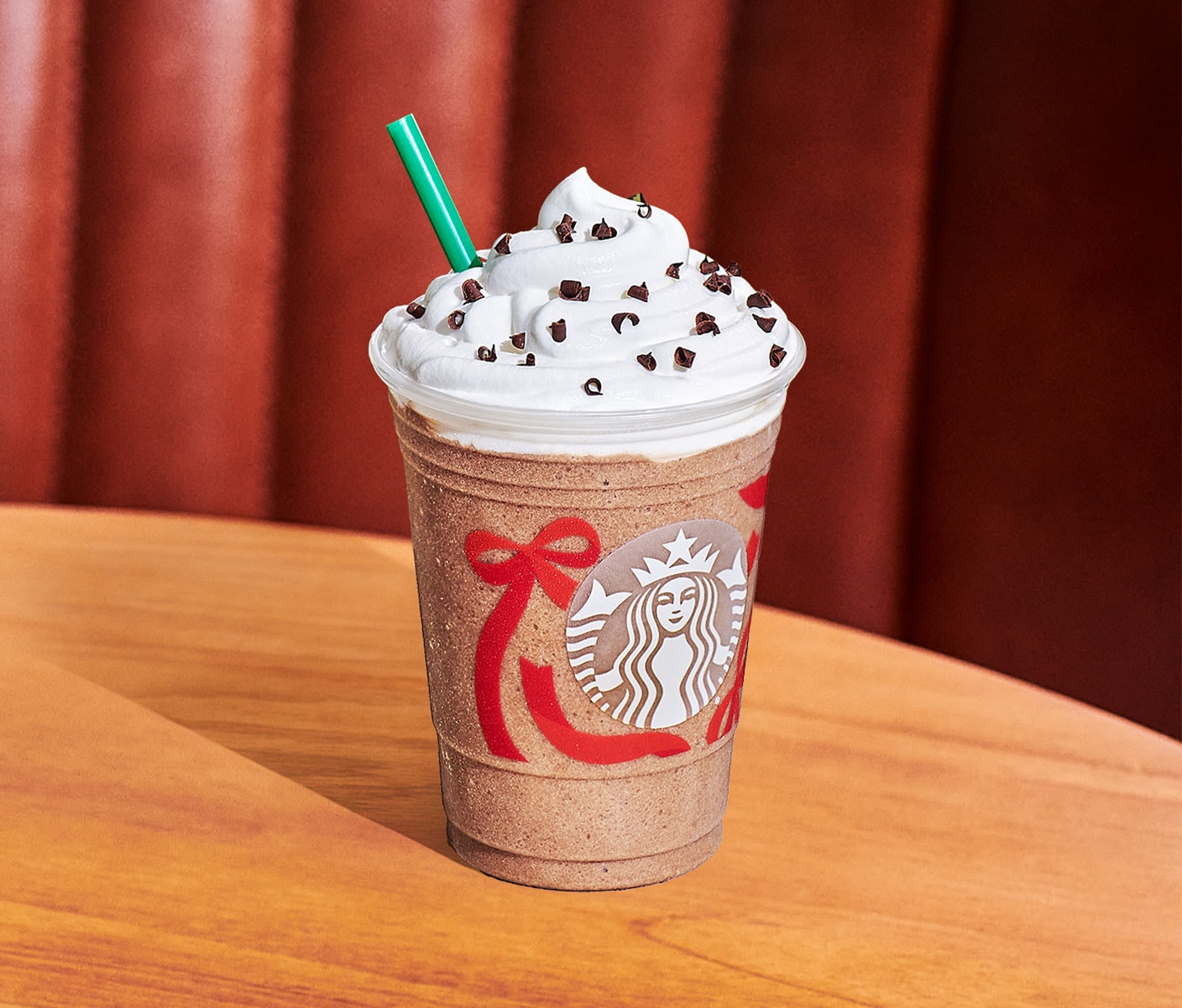 A creamy iced coffee drink with whipped cream and brown sprinkles in a clear Starbucks cup with a red ribbon design and green straw.