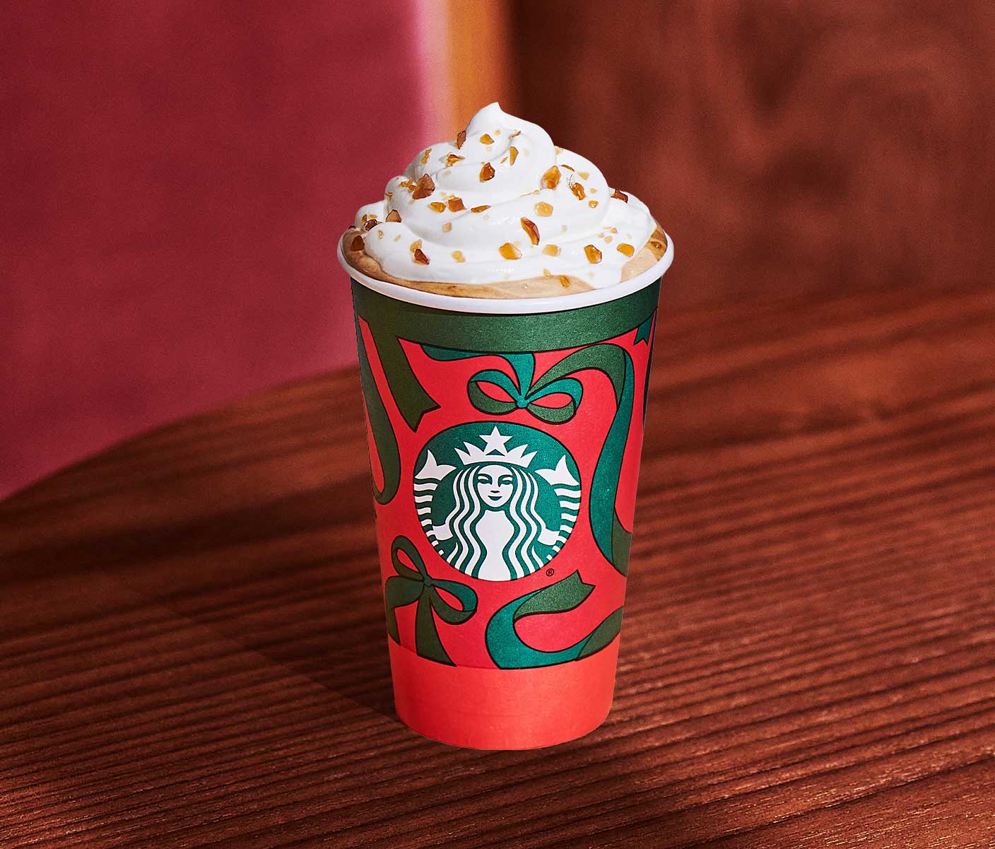 A hot coffee drink with whipped cream and caramel-colored sprinkles in a red and green Starbucks cup.