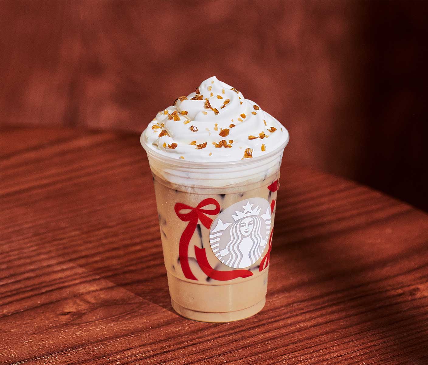 A creamy iced coffee drink with whipped cream and caramel-colored sprinkles in a clear Starbucks cup with a red ribbon design.