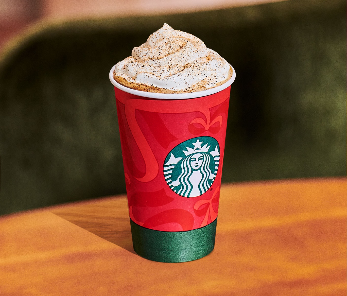 A hot coffee drink with whipped cream and brown spice topping in a red and green Starbucks cup.