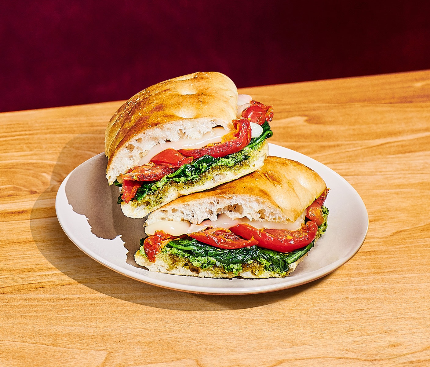 Two halves of a sandwich are stacked on a white plate with each half showing layers of green spinach, red tomato and white cheese.