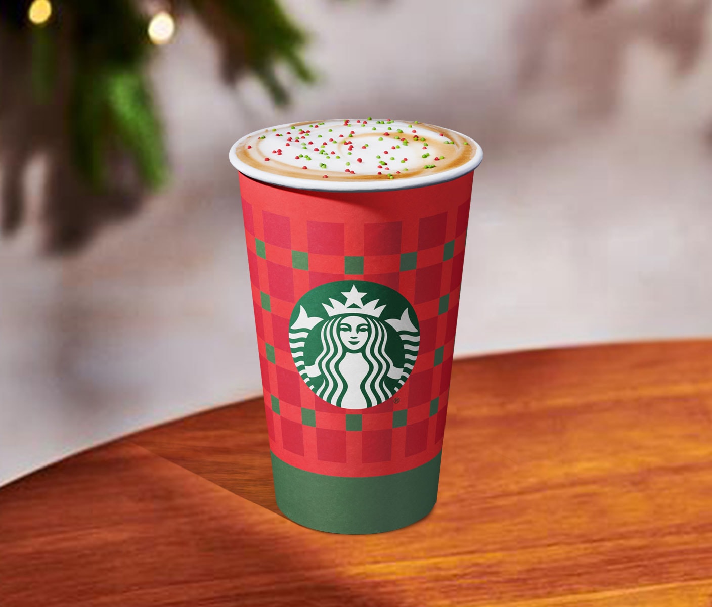 A hot coffee drink with foamy top and red and green sprinkles in a red and green Starbucks cup.