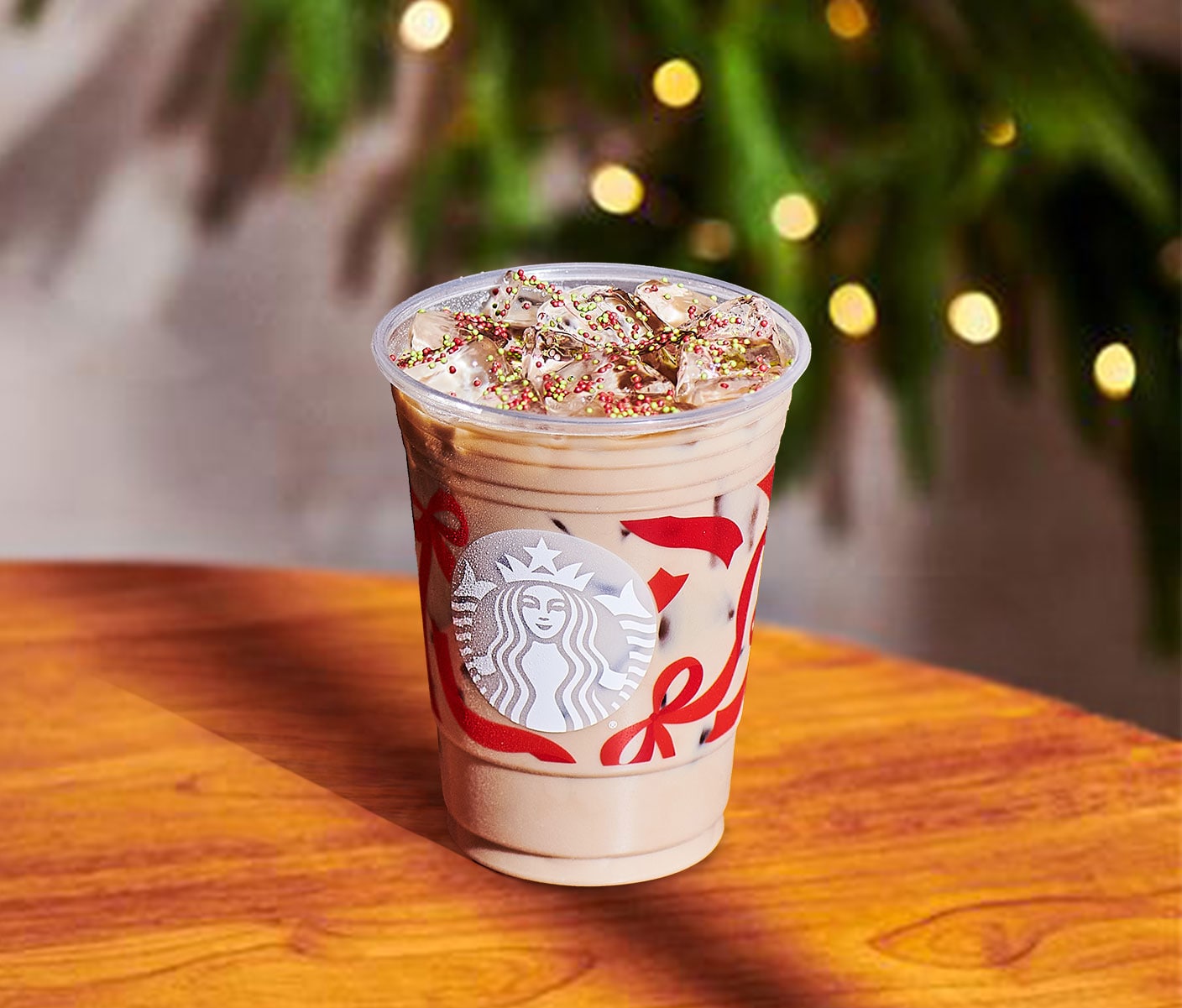 A creamy iced coffee drink with foamy top and red and green sprinkles in a clear Starbucks cup with red ribbon design.