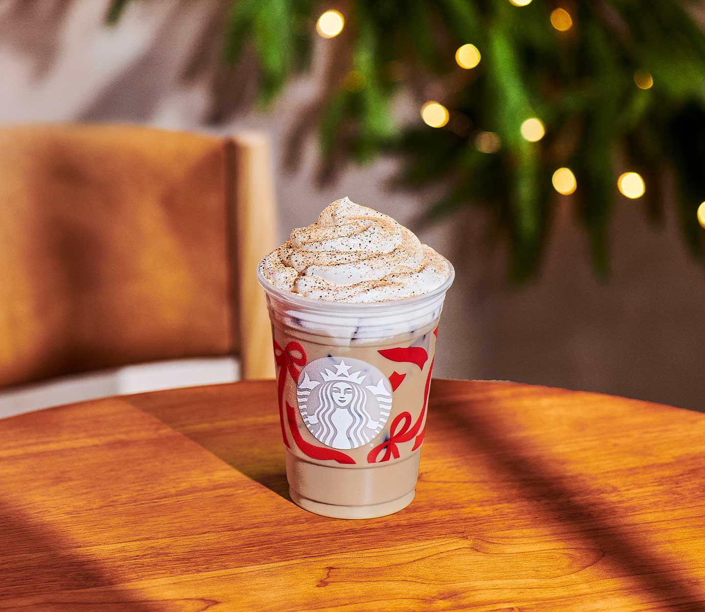 A creamy iced coffee drink with whipped cream and caramel-colored sprinkles in a clear Starbucks cup with red ribbon design.