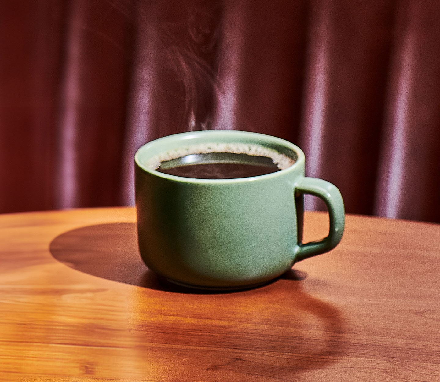 Hot coffee in a green mug sits on a wood table.