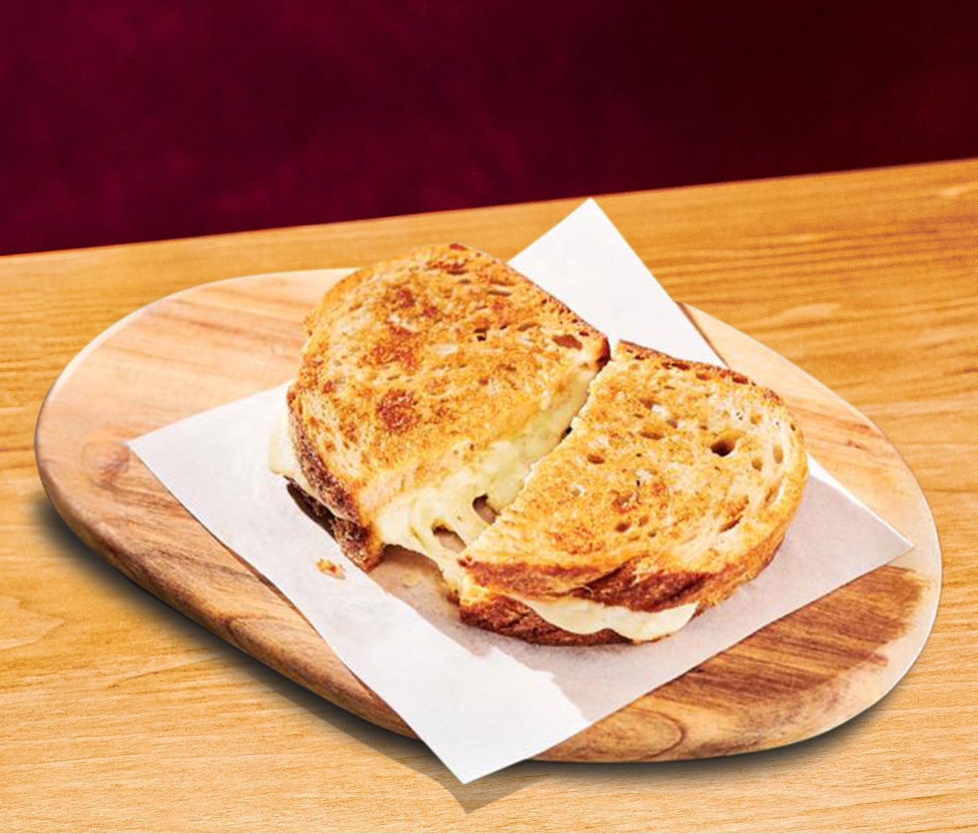 Two halves of a toasted sandwich with oozing melted cheese in the middle is placed on a white napkin on a wooden board. 