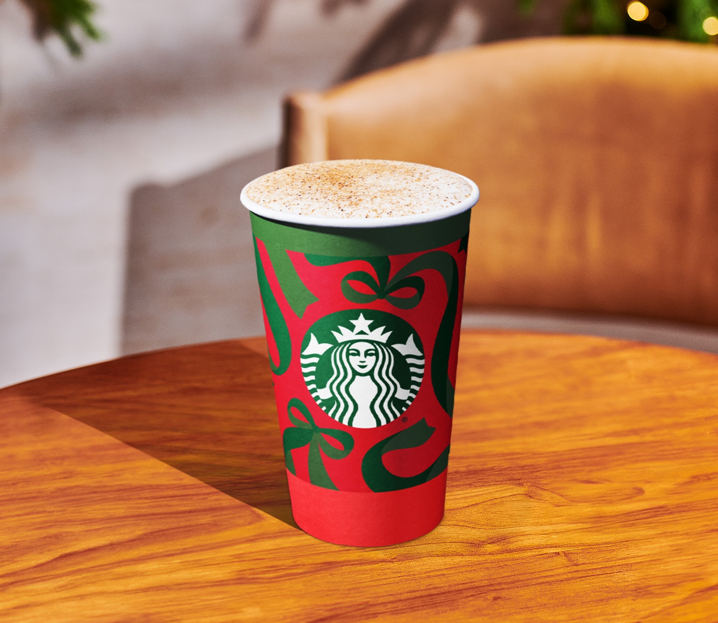 A hot drink with a foamy top and brown sprinkles in a Starbucks holiday cup on a wood table.