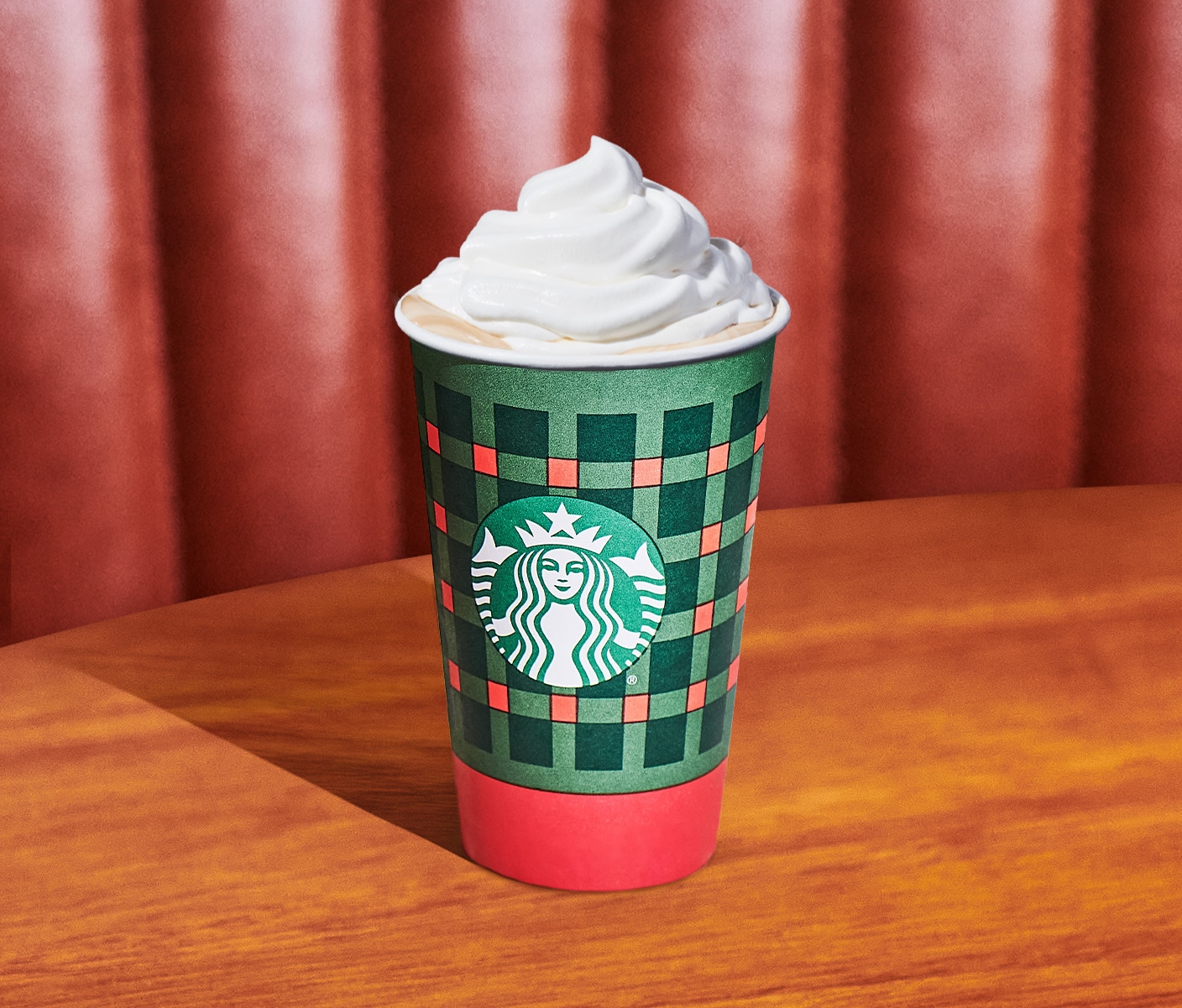 A hot coffee drink topped with whipped cream in a Starbucks cup on a wood table.
