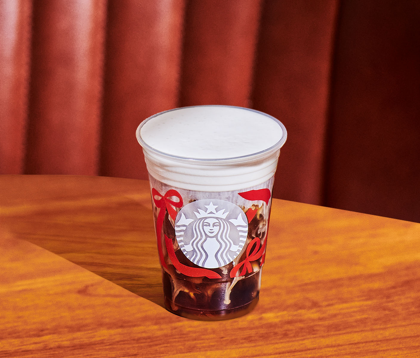 An iced coffee drink with a foamy top in a plastic Starbucks cup on a wood table.