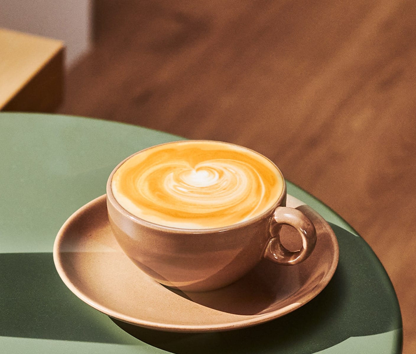 A hot coffee drink with a foamy top in a mug on a saucer on a table.