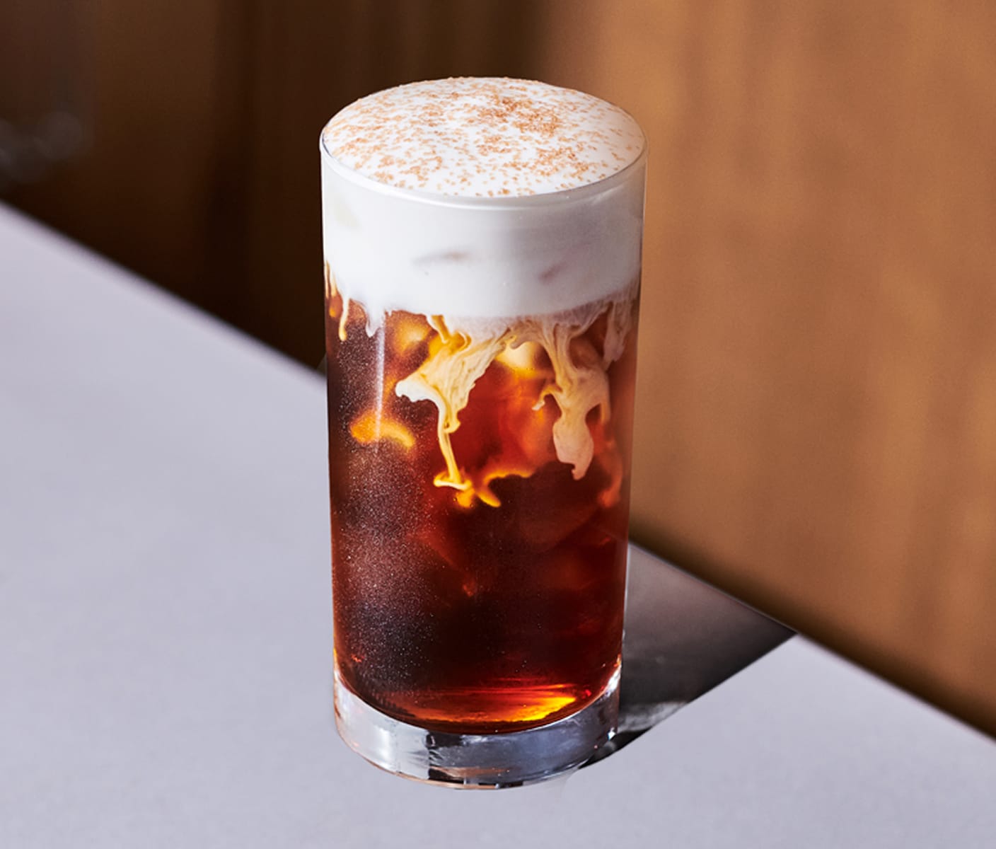 A creamy iced coffee drink with cascading foamy top in a tall glass.