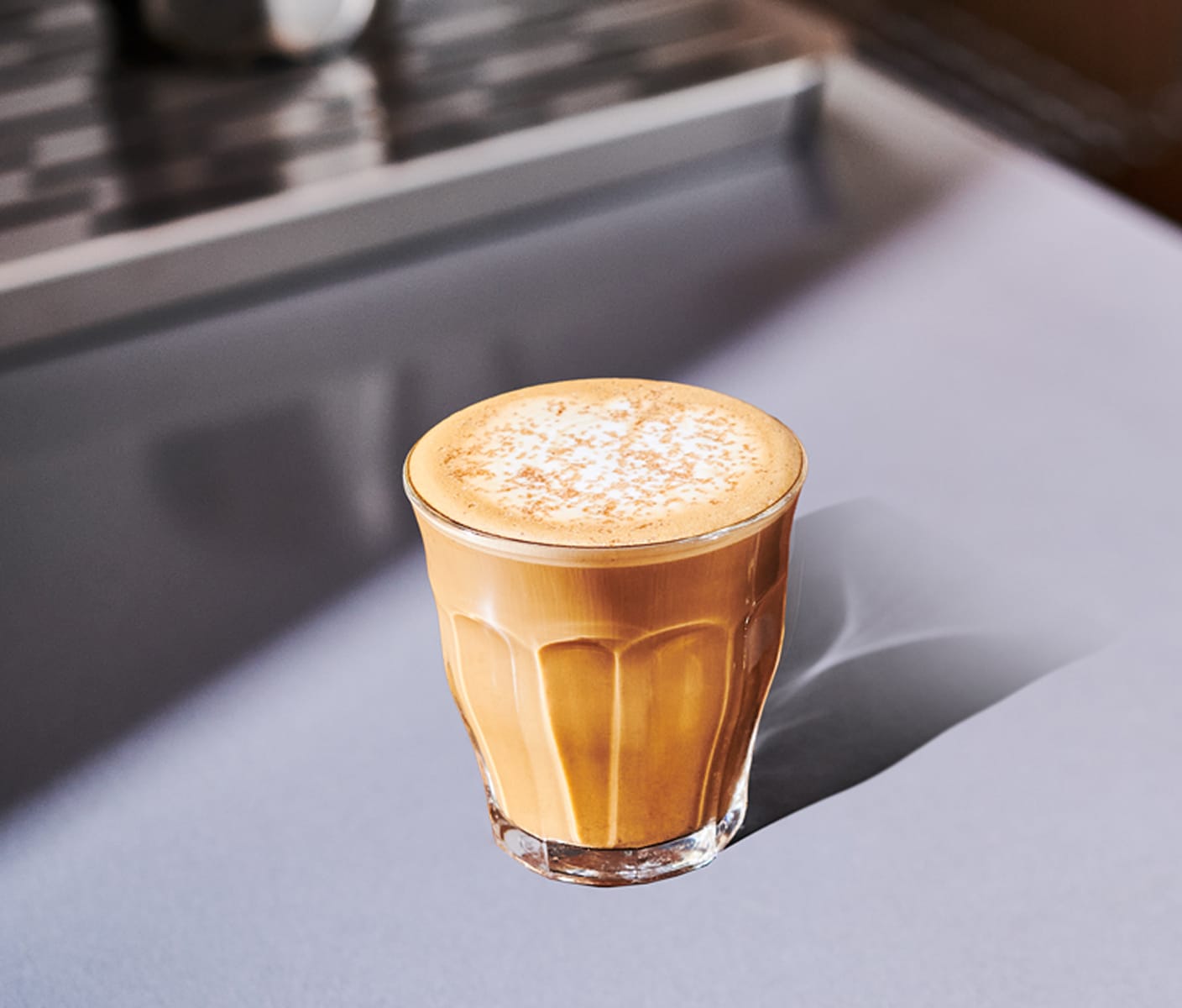 A creamy coffee drink in a small glass with foamy top and sprinkles.