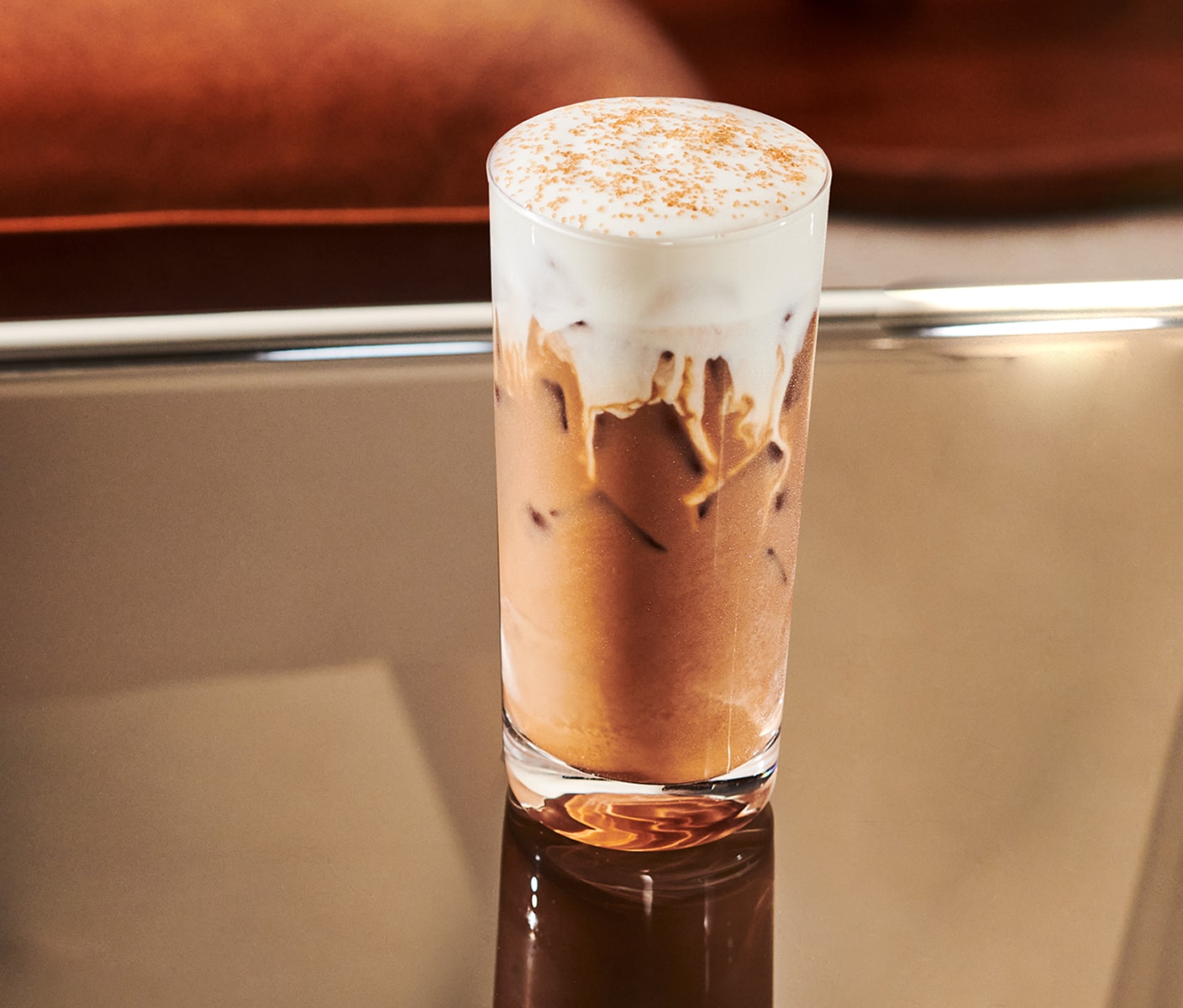 A creamy iced coffee drink with thick foam and sprinkles in a tall glass.