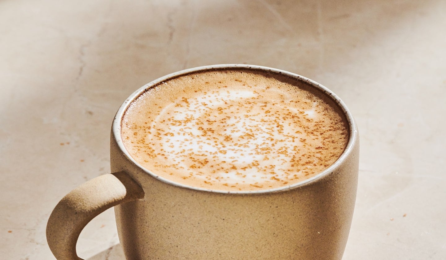 The top half of a mug of hot coffee with foamy top and sprinkles.