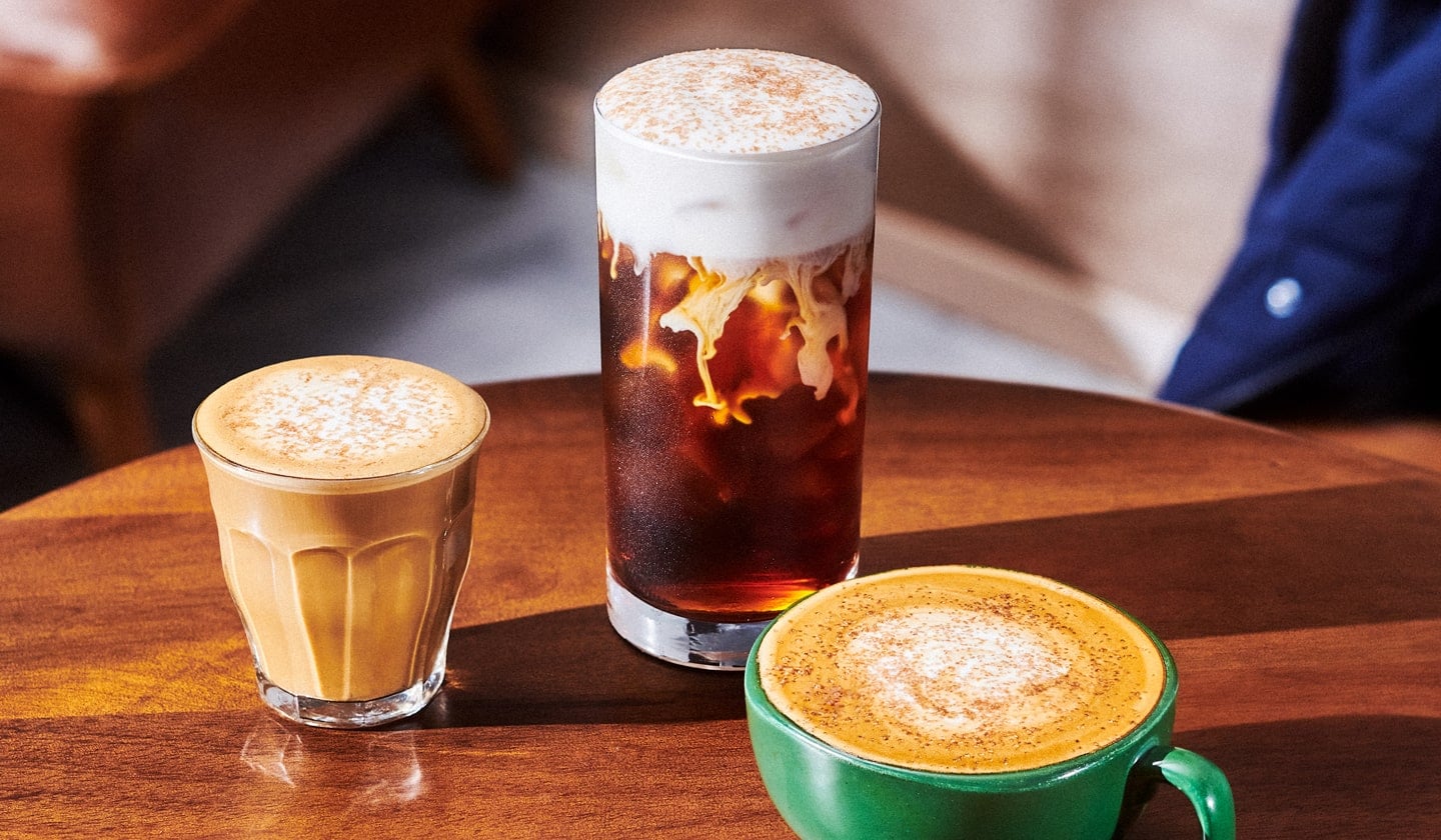 A small creamy coffee drink in a glass next to a tall iced coffee drink with a foamy top in a glass and a hot coffee drink with foamy top in a mug—all with sprinkles on top.