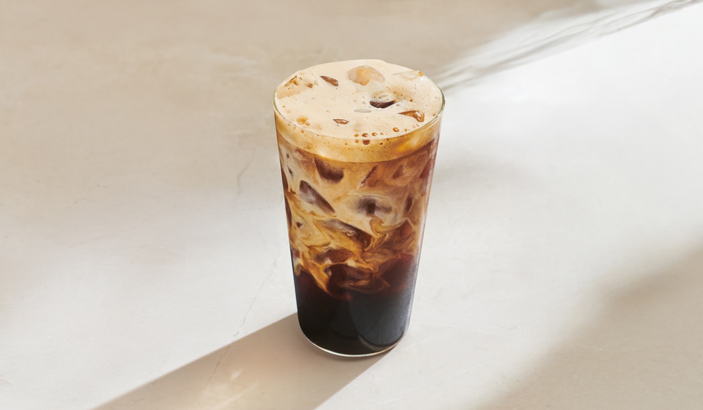 A Brown Sugar Oatmilk Iced Shaken Espresso in a tall glass on a beige table.