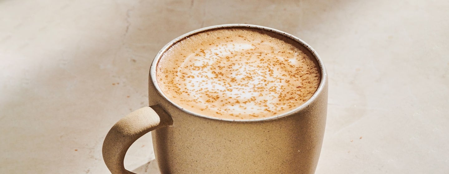 The top half of a mug of hot coffee with foamy top and sprinkles.