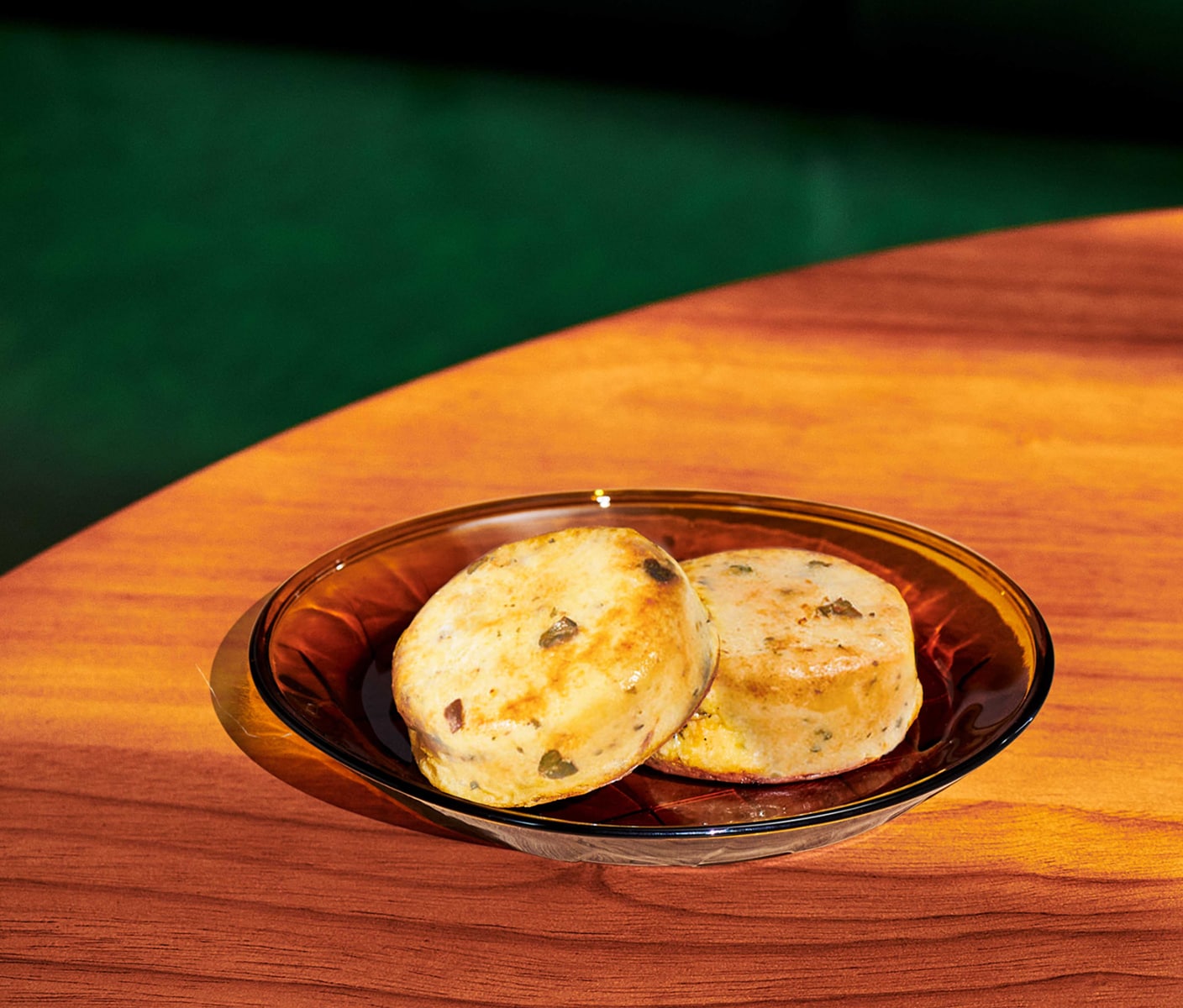 Two round egg-mixture forms with bits of vegetables and herbs and a fork on a round plate on a wooden table.