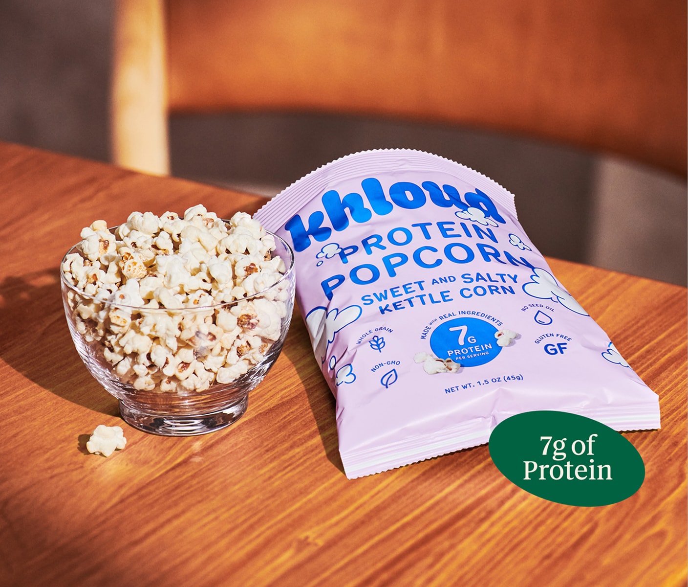 Close-up shot of a bowl of popcorn next to a bag of Khloud popcorn, resting on top of a wooden table.