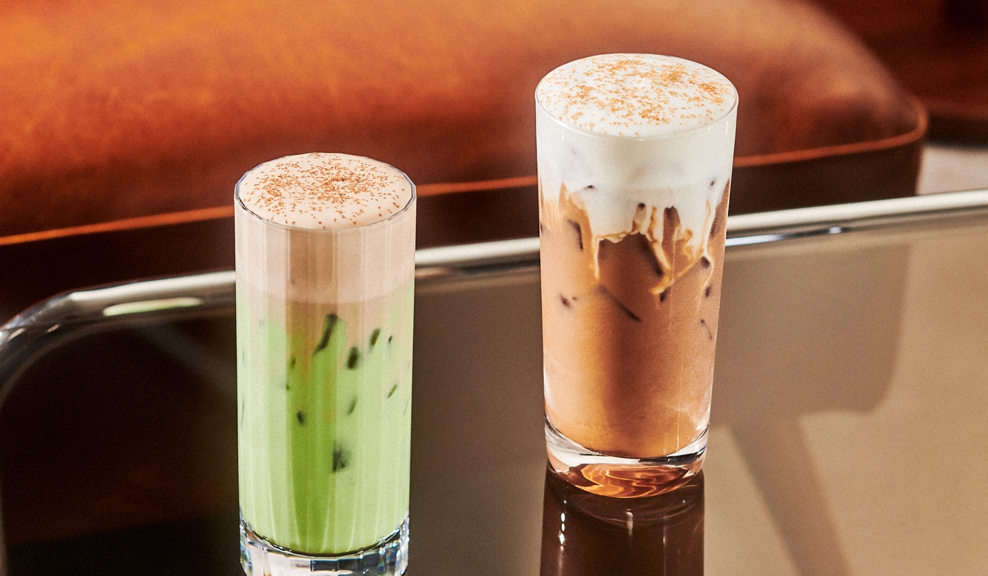 Two iced drinks in glasses with thick foamy toppings. One is a creamy tea and the other a creamy coffee.