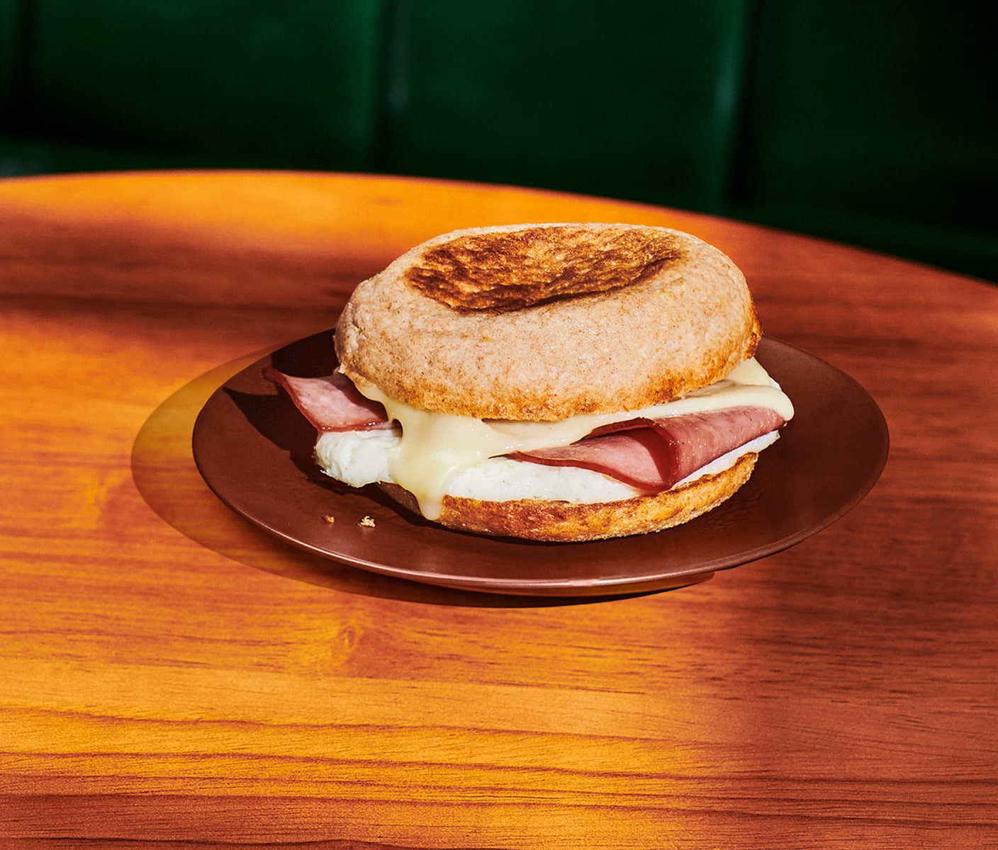 A close up of a breakfast sandwich with layers of egg, meat and melted cheese between two slices of toasted bread.