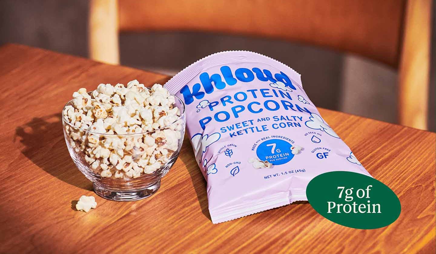 Close-up shot of a bowl of popcorn next to a bag of Khloud popcorn, resting on top of a wooden table.