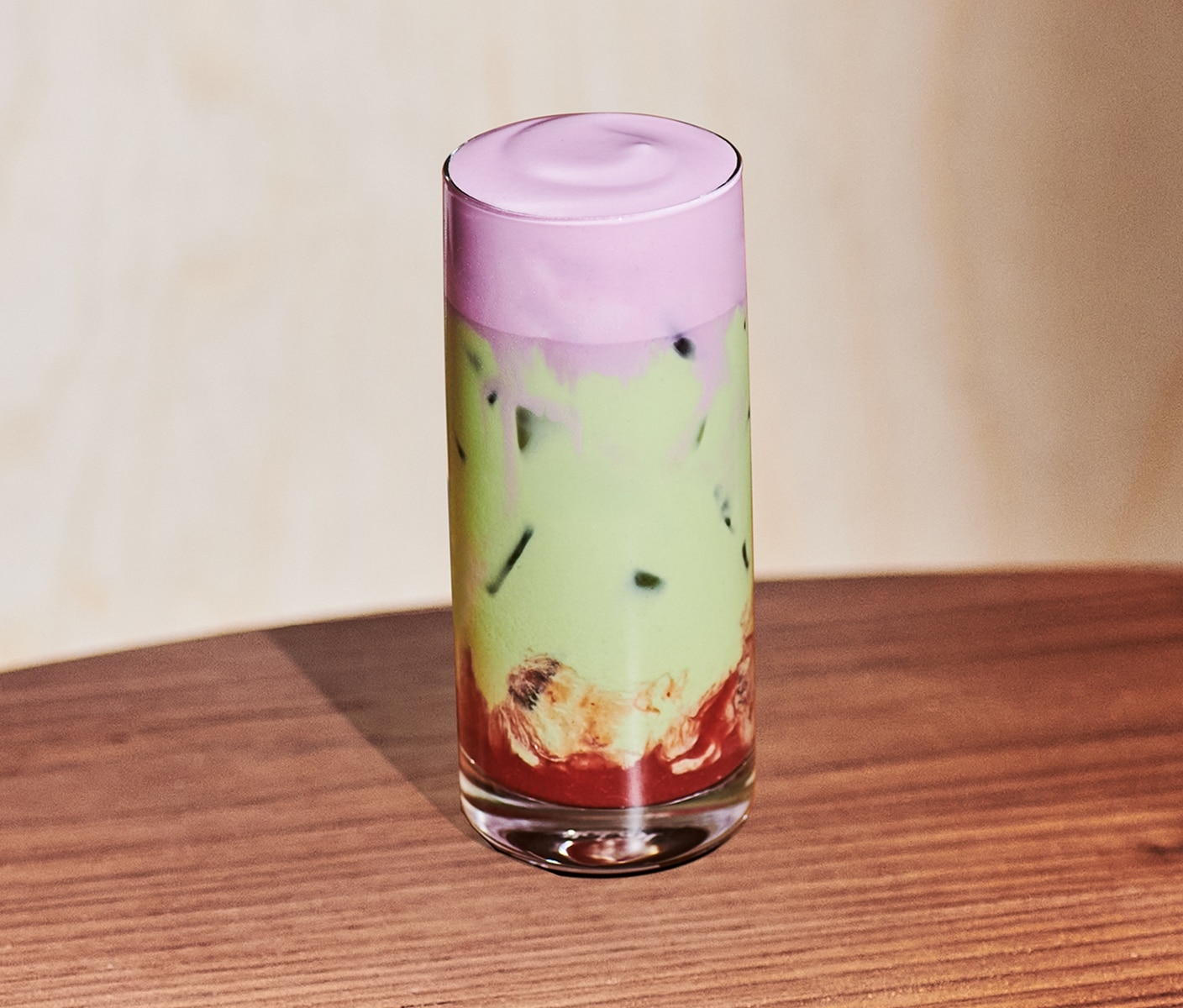 An iced creamy tea drink in a glass with a bottom layer of berry puree and top layer of foam.