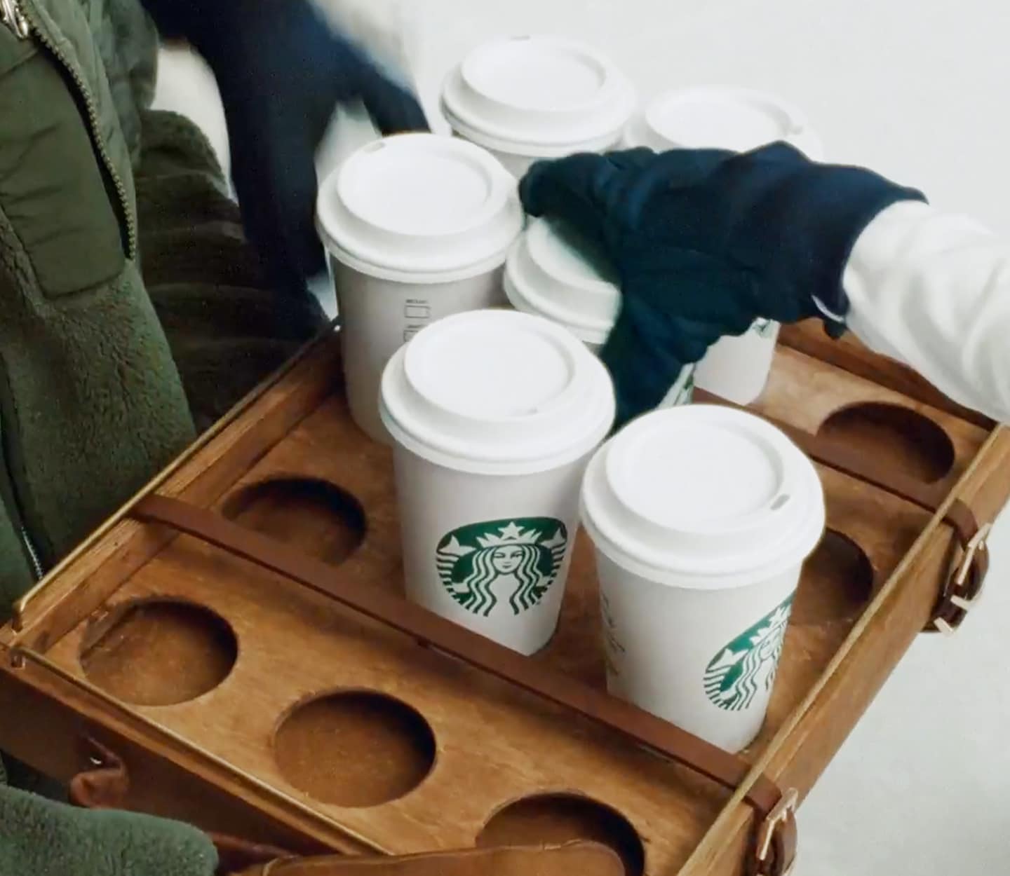 A hand reaches for a Starbucks drink from a full drink carrier.