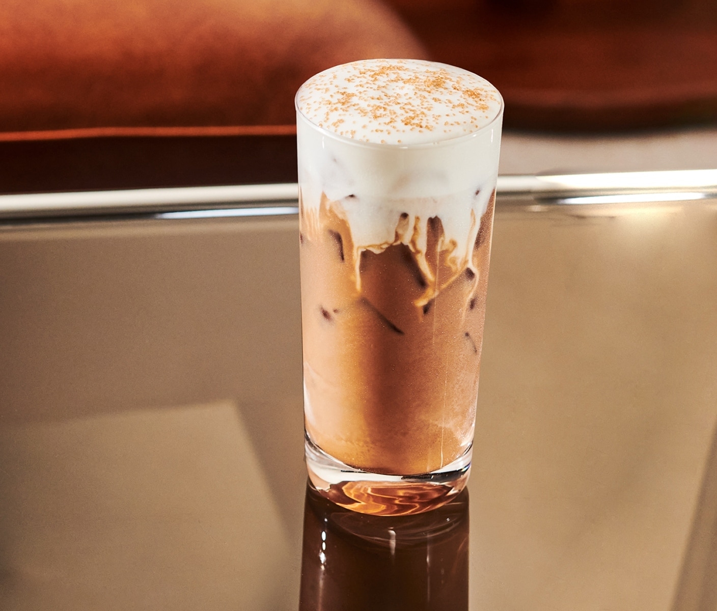 A creamy iced coffee drink with thick foam and sprinkles in a tall glass.