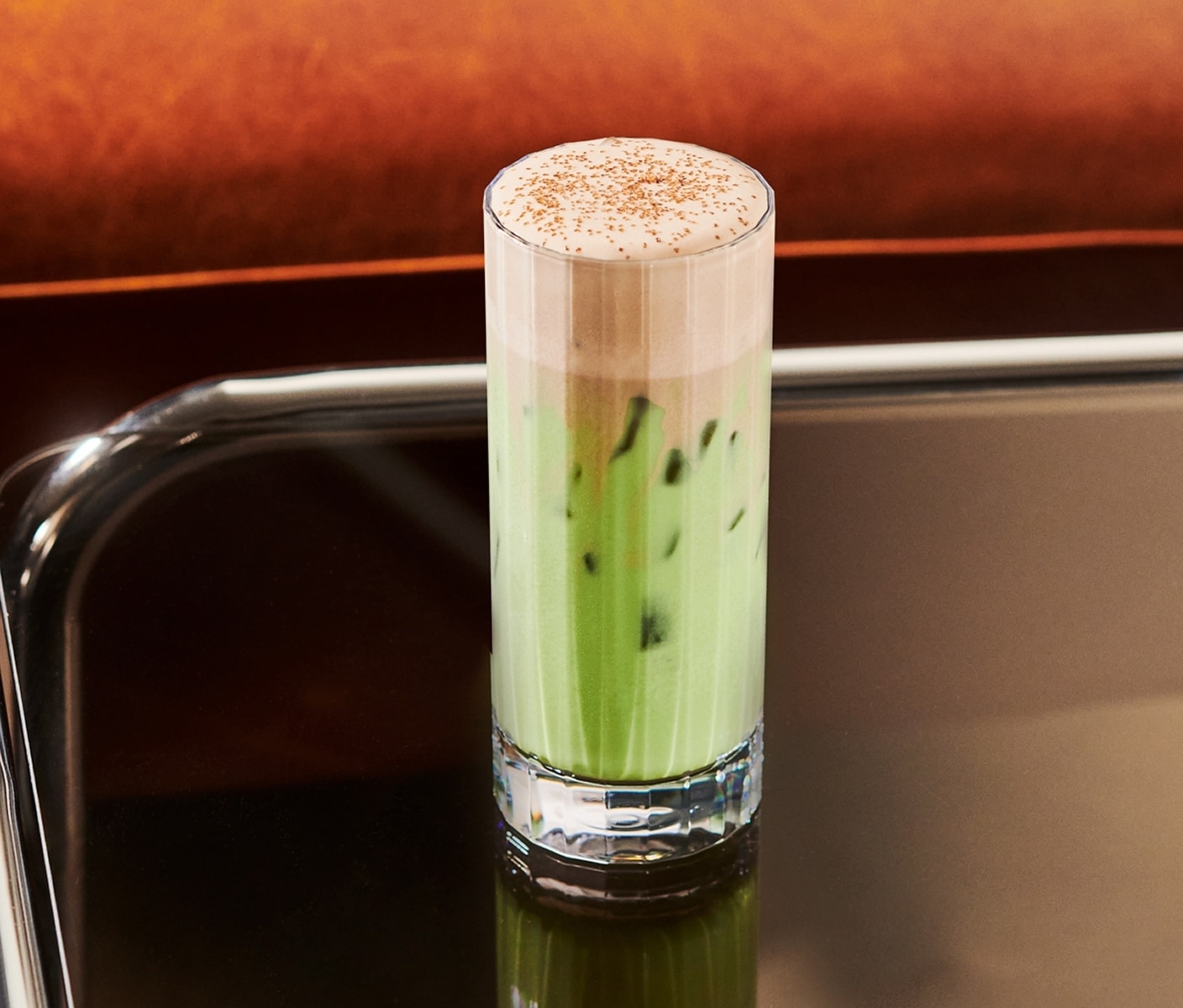 A creamy iced tea drink with thick foam and sprinkles in a tall glass.