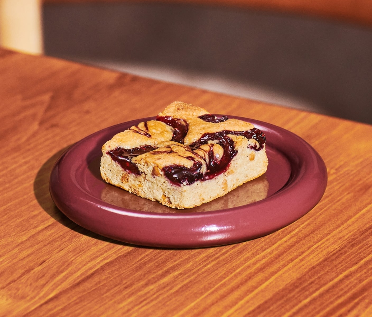 A square dessert bar with chocolate pieces and swirls of jam on a plate.