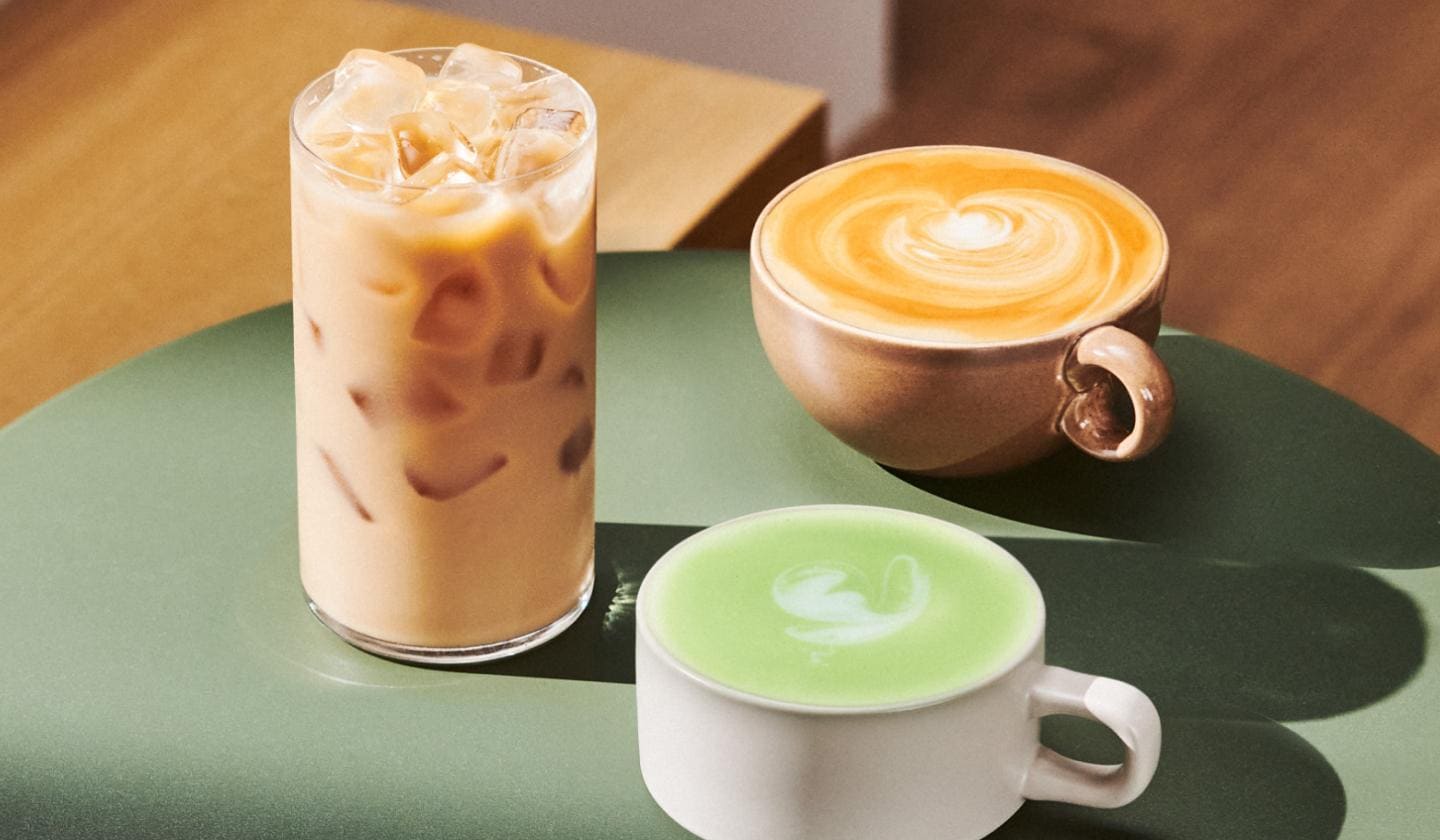 An iced coffee drink in a glass next to a hot coffee drink and hot tea drink, both with foam and in mugs.