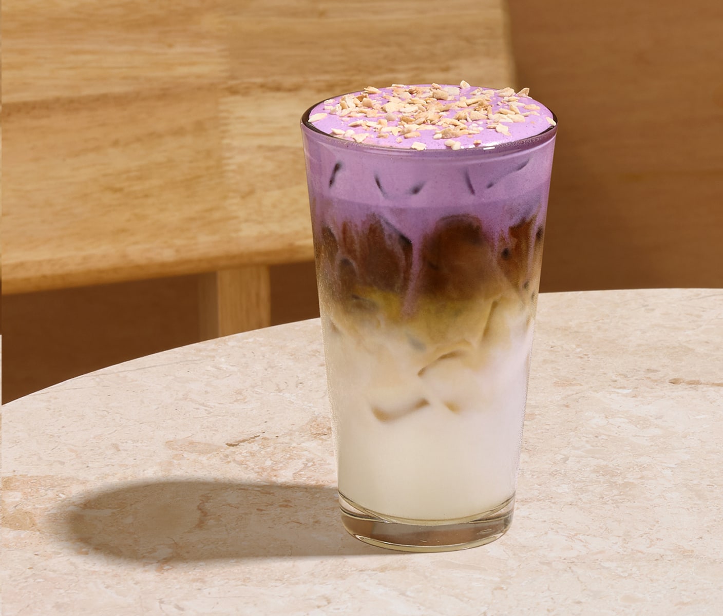 In iced coffee drink in a glass with a creamy bottom layer, middle coffee layer and foamy top with sprinkles.