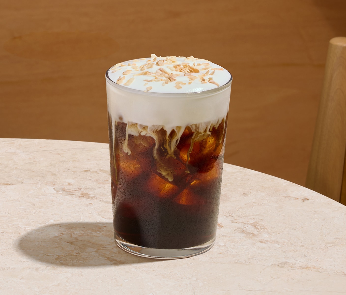 An iced coffee drink in a glass with a thick foamy top and sprinkles.