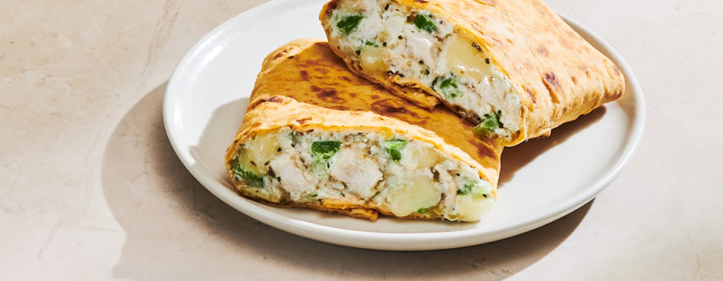 A stack of two flatbread sandwich halves revealing a creamy chicken and peppers filling.