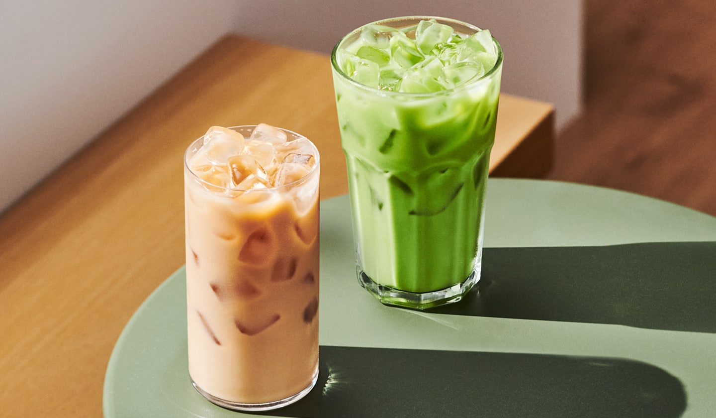 A glass of creamy iced coffee next to a glass of creamy iced tea.