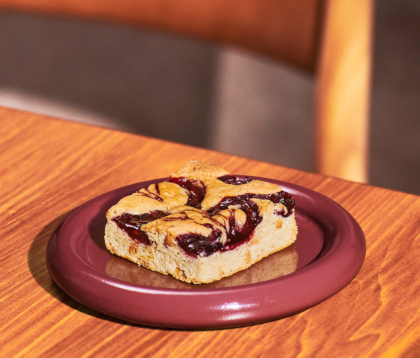 A square dessert bar with swirled jam on top on a plate.