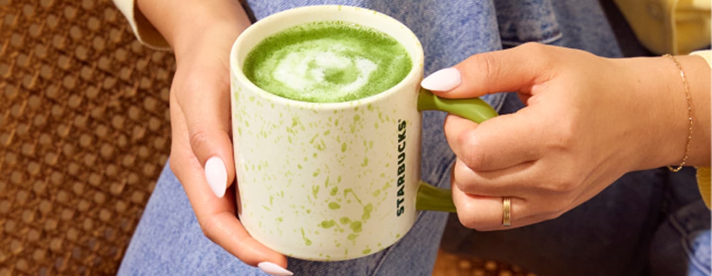 A pair of hands holds a mug filled with creamy foamed matcha.