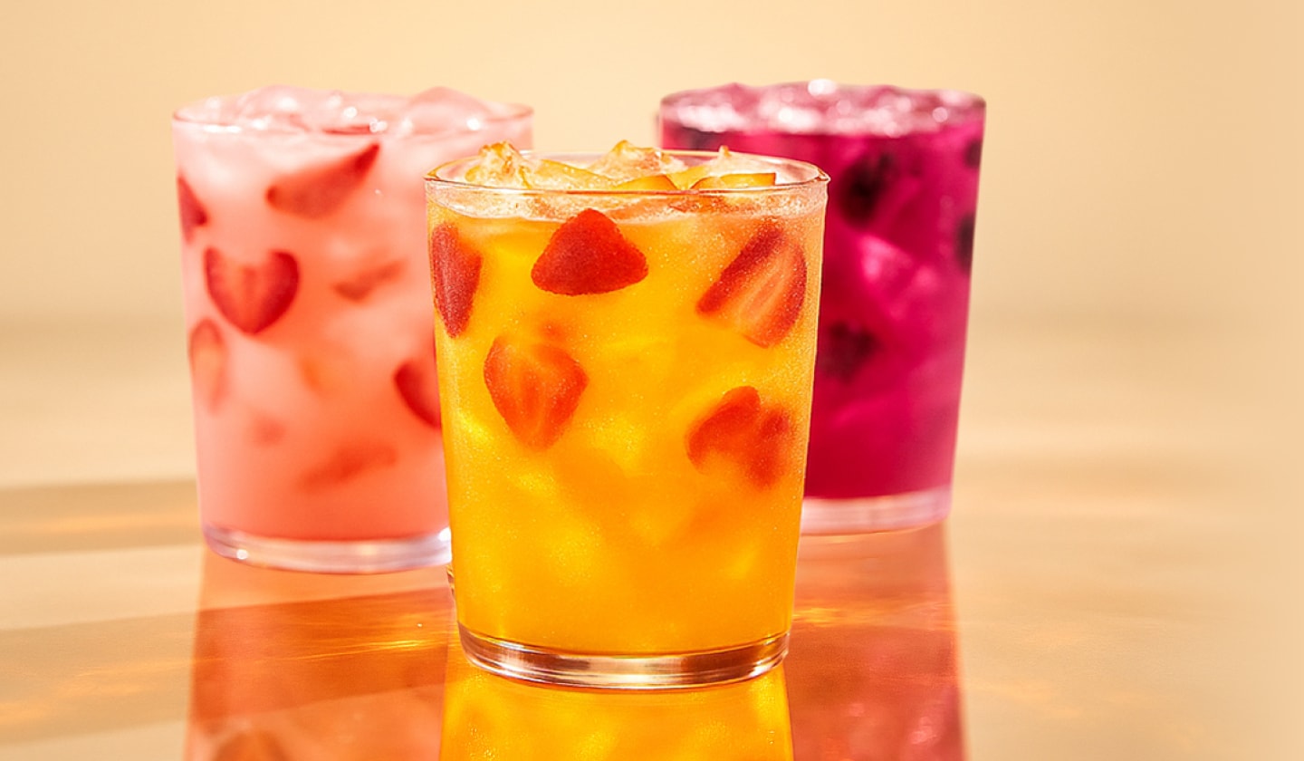 Three Energy Refreshers in glasses sit on a reflective surface against a peach-colored background.