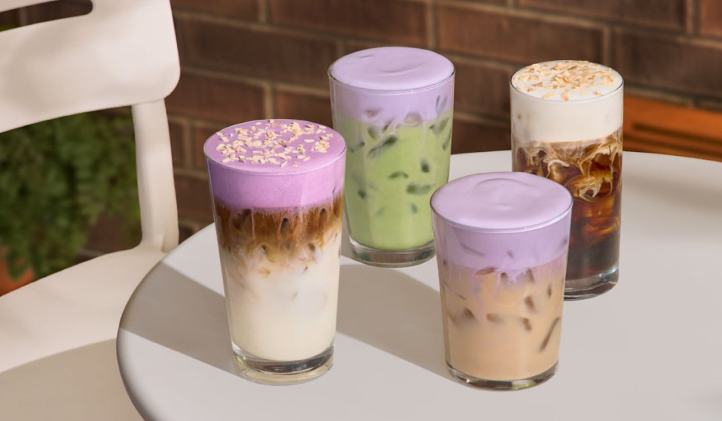 Four iced beverages sit on a white table: Iced Ube Coconut Macchiato, Iced Lavender Cream Chai, Iced Lavender Cream Matcha and Toasted Coconut Cream Cold Brew.