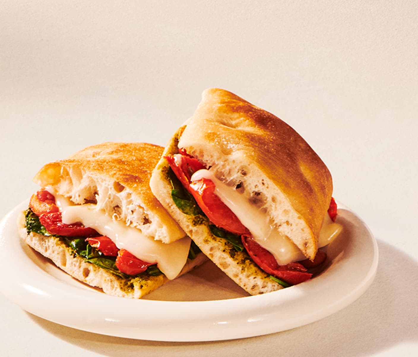 Two halves of a sandwich stacked on a plate, revealing layers of spinach, tomato and melted cheese.