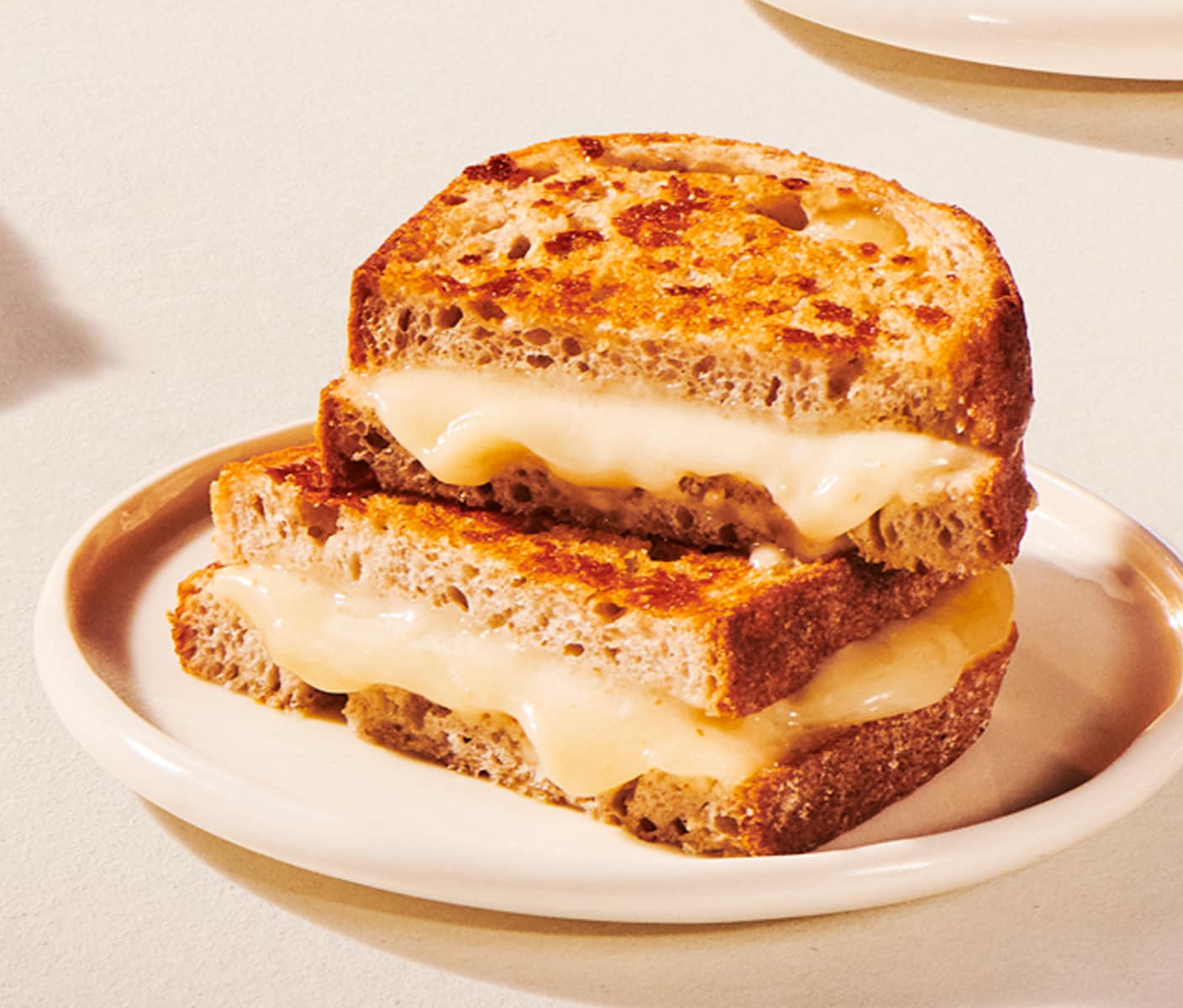 Two halves of a toasted sandwich with oozing melted cheese are stacked on a plate.